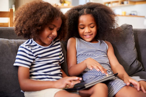 istock Brother And Sister Sitting On Sofa At Home Playing With Digital Tablet 1156463224