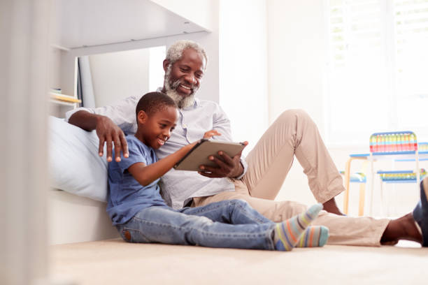 grand-père s'asseyant avec le petit-fils dans la chambre d'enfant utilisant la tablette numérique ensemble - bed child smiling people photos et images de collection