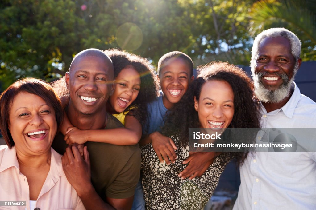 Retrato al aire libre de la familia de varias generaciones en el jardín en casa contra el sol abrasador - Foto de stock de Familia libre de derechos