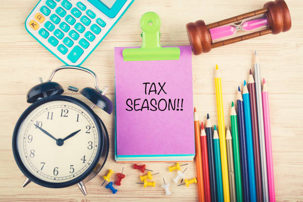 istock working table with calculator, clock, hourglass and Tax Season word written on notepad 1156466253