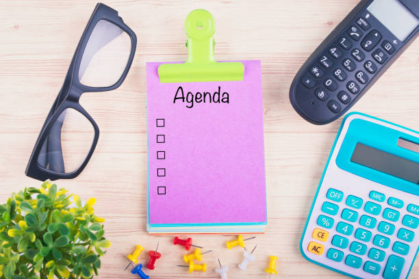 istock Notepad writing AGENDA, Office table with calculator, telephone, eyeglass and thumbtacks 1156466419