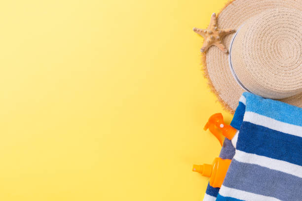 istock Beach flat lay accessories with copy space. Striped blue and white towel, seashells, staw sunhat and a bottle of sunblock on yellow background. Summer holiday concept 1156468265