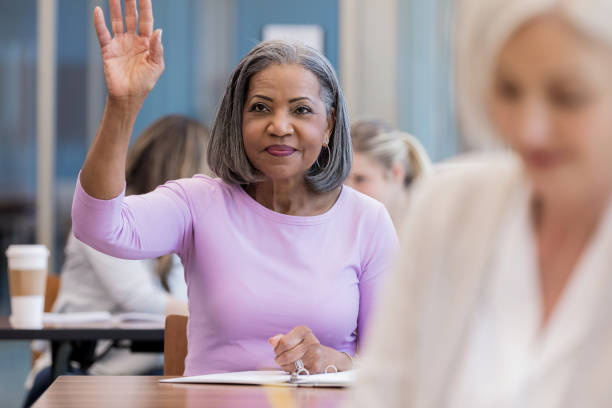 Attractive mature African American woman raises hand in class An attractive mature African American woman asks a question by raising her hand in class. middle age adult studying stock pictures, royalty-free photos & images