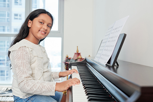Portrait of student playing the piano and smiling at camera during her lesson at musical school