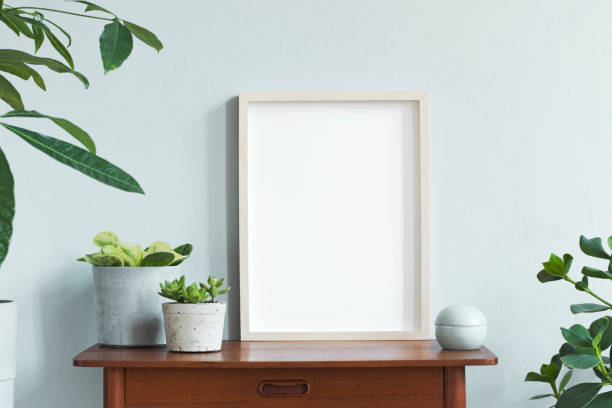 istock Stylish scandinavian interior with design retro table, white mock up photo frame and beautiful plants in design pots and accessories. Modern home decor. Gray background wall. Minimalistic concept. 1156475166