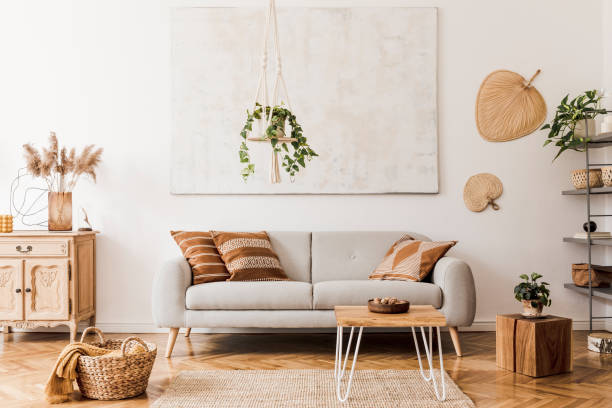 The stylish boho interior of open room in cozy apartment withdesign furnitures and elegant personal accessories. Template. Home decor. Honey yellow concept. la elegante composición boho en el interior de la sala de estar con sofá gris de diseño, mesa de centro de madera, cómodo y accesorios personales elegantes. almohada amarilla de miel y a cuadros. acogedor apartamento. decoración del hogar