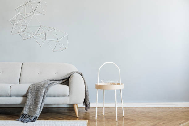 istock Minimalistic and abstract interior of open space with design gray sofa, coffee table, triangle geometric sculptures. Gray background walls, brown wooden parquet. Modern concept of room. Template. 1156479335