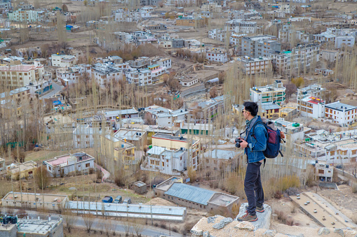 Traveler man standing on Leh Ladakh city view from Shanti Stupa. Beautiful amazing village in the valley with snow mountain at background. Ladakh, India.