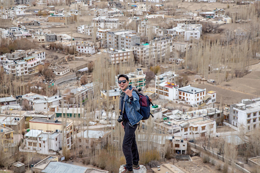 Traveler man standing on Leh Ladakh city view from Shanti Stupa. Beautiful amazing village in the valley with snow mountain at background. Ladakh, India.