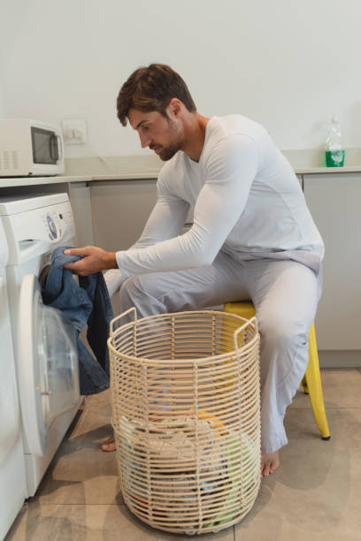 istock Man putting clothes in washing machine at home 1156479949