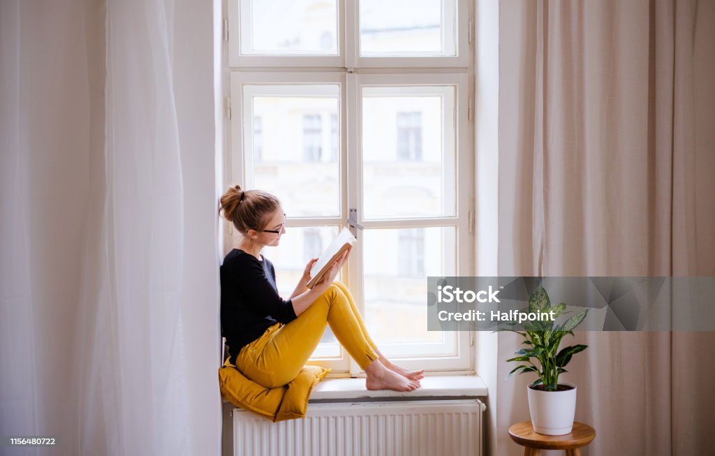 창틀에 앉아 공부하는 책을 들고 있�는 젊은 여학생. - 로열티 프리 읽기 스톡 사진
