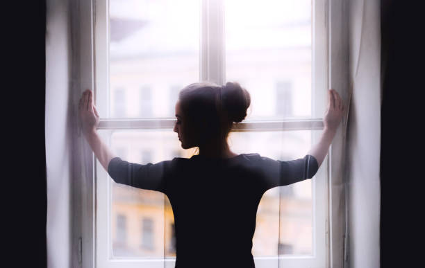 istock Rear view of young sad female student standing by window. 1156480735