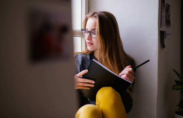 istock A young female student with an exercise book sitting on window sill, studying. 1156480753