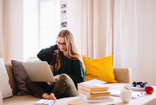 Una joven estudiante sentada en el sofá, usando computadora portátil cuando estudia. photo