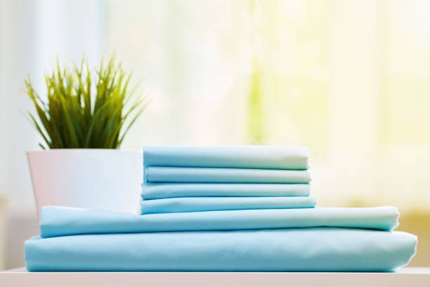 istock Closeup of blue clean bedding on a blurred background. A stack of folded new bed sheets on the table. Sunlight from the window. 1156481430
