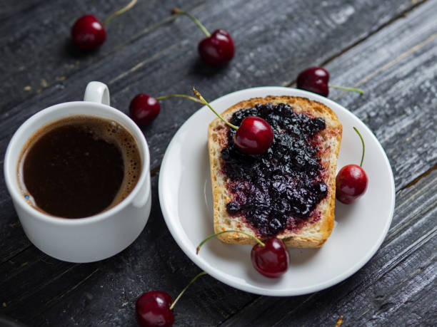 istock White Cup of coffee and toast with cherry jam on white plate on black table 1156482112