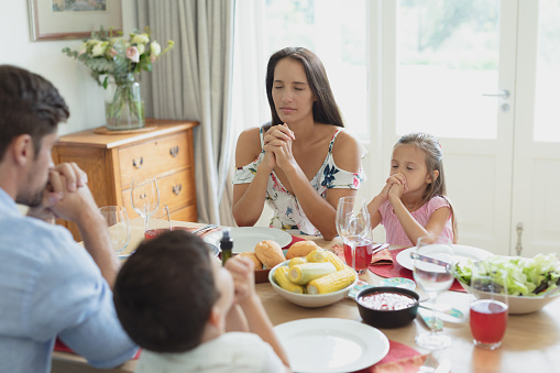 Front view of Caucasian family praying together before having lunch at dining table in comfortable home