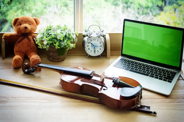 The classic violin and bow put on wooden desk,beside laptop and alarm clock.