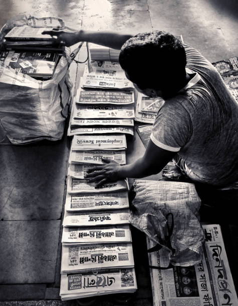 An Indian newspaper vendor Monochromatic high angle view of an Indian newspaper vendor, selling daily newspapers at a railway station platform in Kolkata. He is arranging newspapers of different names on platform floor, and those newspapers are in different languages also, mostly Bengali, English and Hindi.
Kolkata being a multicultural, multi-language spoken city, it is very normal to see multi-language printed medias in book/magazine stores.
Photo taken at Kolkata on 05/06/2017. newspaper seller stock pictures, royalty-free photos & images