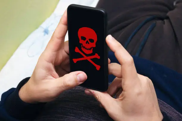 Photo of man is holding a phone hacked in his hand. The red skull burns on the modern screen and indicates a serious danger. Flat style. A man is holding a phone hacked