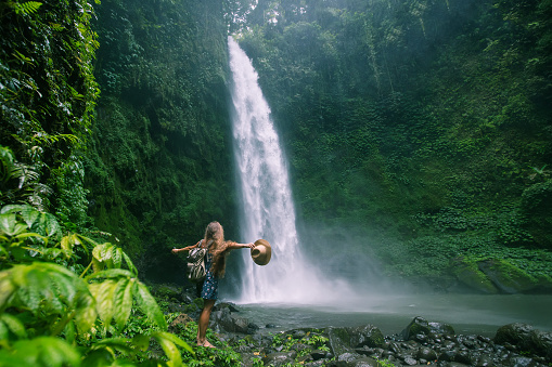 Attractive young woman gazing up at large waterfall with lush foliage in soft golden light. Shot in Tennessee, USA.