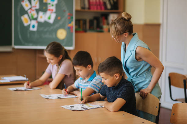 istock Teacher helping school kids writing test in classroom. education, elementary school, learning and people concept 1156495140