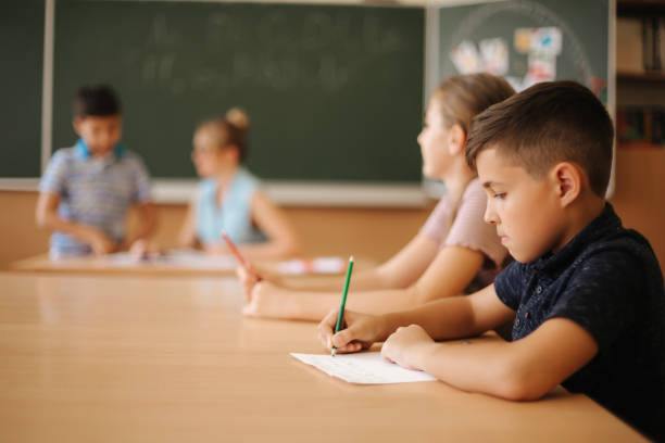 istock Education, elementary school. Learning and people concept - group of school kids with pens and notebooks writing test in classroom 1156498683