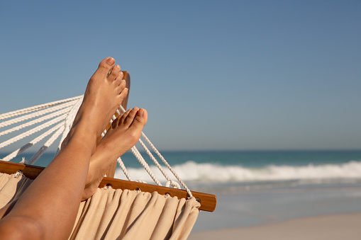 Low section of African american woman relaxing on hammock at beach in the sunshine