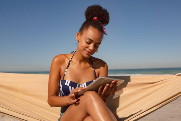 istock Woman using digital tablet while sitting on hammock at beach in the sunshine 1156499450