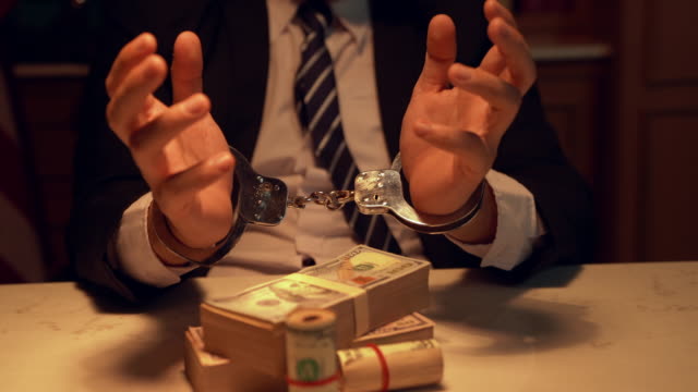 Businessman in handcuffs holds money arrested. Businessman in office in handcuffs holding a bribe of euro banknote. Arrested terrorist. Financial crime, dirty money and corruption concept. Selective focus.