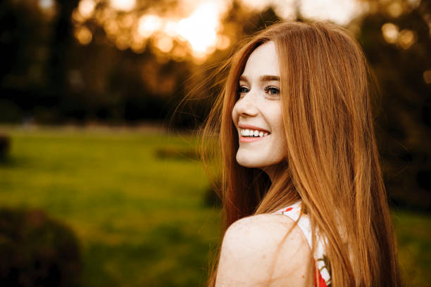 retrato de uma fêmea encantadora com cabelo e os sardas vermelhos longos que olham afastado rindo de encontro ao por do sol fora. - long red hair - fotografias e filmes do acervo