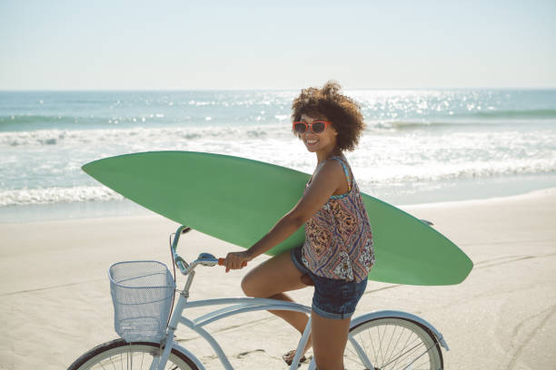 istock Woman holding a surfboard with bicycle at beach 1156509503