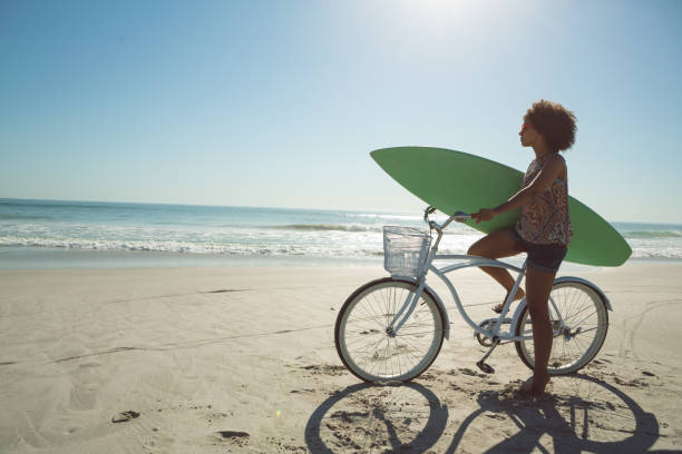 istock Woman holding a surfboard with bicycle at beach 1156509540