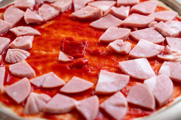 pizza dough smeared with ketchup and with slices of sausage as background