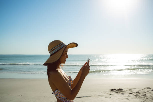 istock Woman in hat using mobile phone on the beach 1156510935