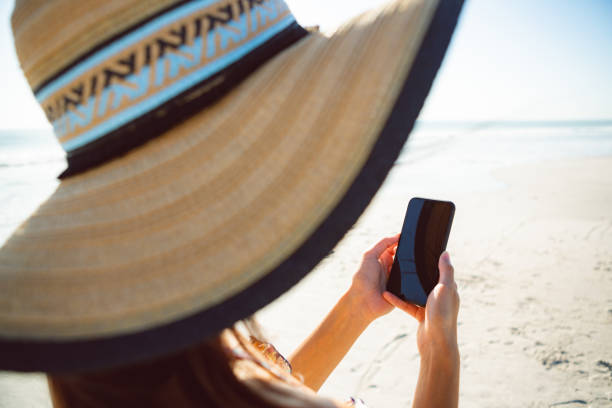 istock Woman in hat using mobile phone on beach 1156510947