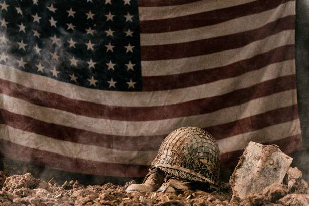 Battlefield memorial for fallen soldier with 48 star US flag A muddy army helmet sitting atop a pair of empty army boots with a pair of dog tags as a memorial to a fallen soldier in battle with a shovel next to them and a 48 star US flag. This could be from World War II or the Korean war. usa flag shoes stock pictures, royalty-free photos & images