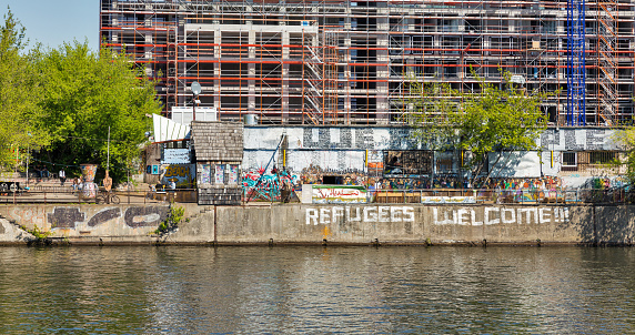 BERLIN, GERMANY - APRIL 18, 2019: People visit YAAM night club with sign Refugees Welcome! along the Spree riverbank. Berlin is the capital and largest city of Germany by both area and population.