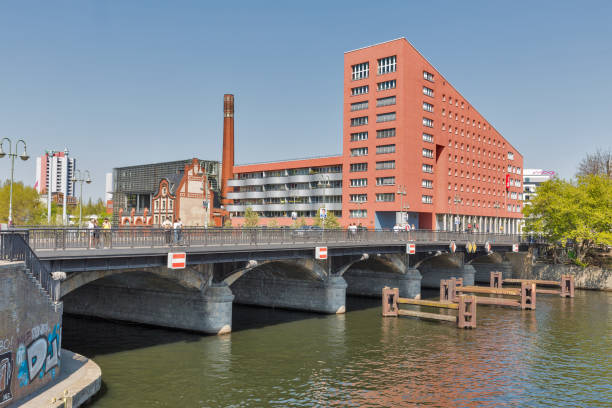 BERLIN, GERMANY - APRIL 18, 2019: People walk along An der Schilling bridge over Spree river. Radialsystem V cultural and event center, European Bible Training Center and Hotel Ibis in the background.
