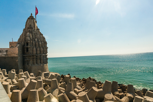 Lone hindu temple with flag on arabian sea coast with wave breakers. The turquoise blue water and blue sky make this holy religious place a perfect tourist and visitor destination. One of the most important towns for hindus