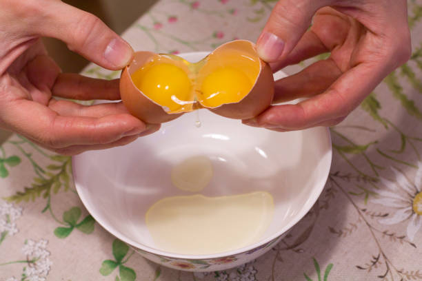 istock Two yolks in one egg. 2 in 1. Women's hands open a unique egg with two yolks. The process of opening eggs for making cake, scrambled eggs, pancakes, muffins. Fashionable ugly food 1156520846
