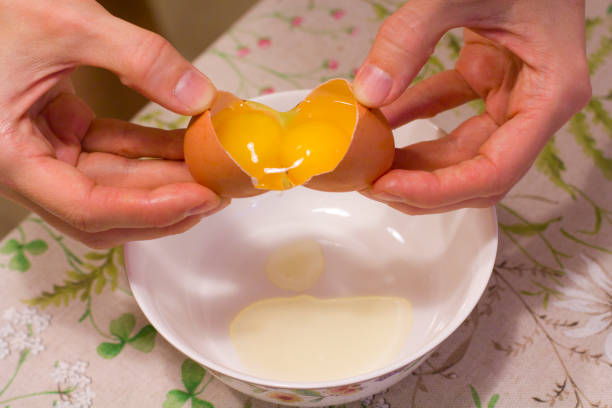 istock Two yolks in one egg. 2 in 1. Women's hands open a unique egg with two yolks. The process of opening eggs for making cake, scrambled eggs, pancakes, muffins. Fashionable ugly food 1156520868