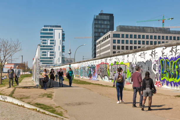 East Side Gallery in Berlin, Germany. BERLIN, GERMANY - APRIL 18, 2019: People visit Wall barrier and East Side Gallery, international memorial for freedom along Spree river at sunny day. friedrichshain photos stock pictures, royalty-free photos & images