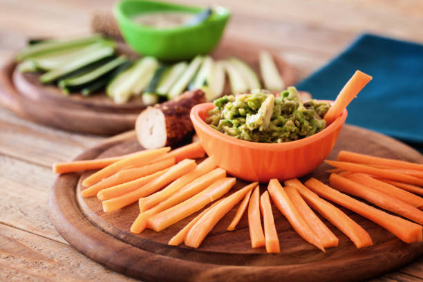 Healthy breakfast, raw carrots, cucumbers sliced into sticks with mash avocado and frozen yogurt at table, close-up
