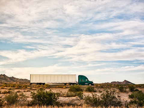 Large semi truck hauling freight on the open highway in the western USA under an evening sky.