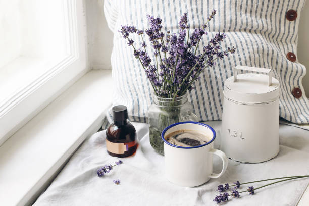 verão francês ainda vida. a chávena de café, alfazema floresce o ramalhete, frasco de óleo da essência no windowsill. foto de stock estilizado feminina, composição floral com ervas dos officinalis de lavandula. cena rústica. - bedding cushion purple pillow - fotografias e filmes do acervo