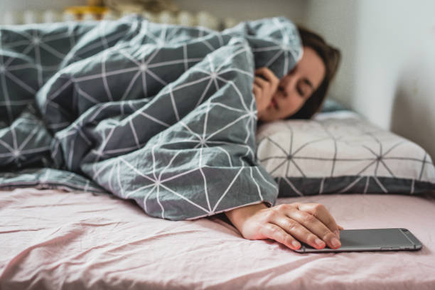 una joven despierta la cama. la alarma en el teléfono inteligente está sonando - sleeping insomnia alarm clock clock fotografías e imágenes de stock