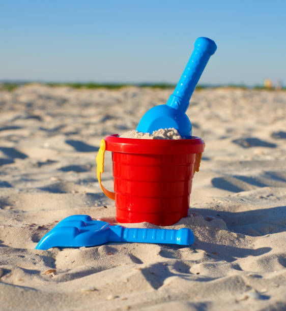 istock red plastic bucket and blue rake, shovel on the sand 1156535193