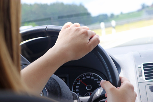 hands of a young woman steering a car through a curve, close-up