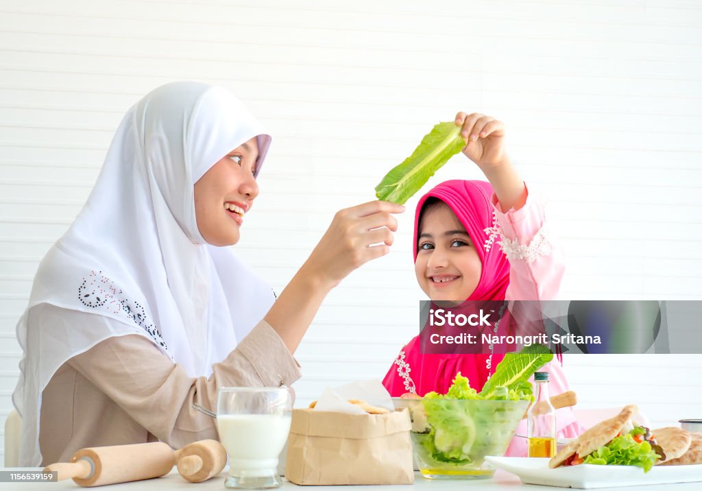 Muslim mother discuss and teach about vegetable for food to her little girl with white background Muslim mother discuss and teach about vegetable for food to her little girl with white background. Adult Stock Photo